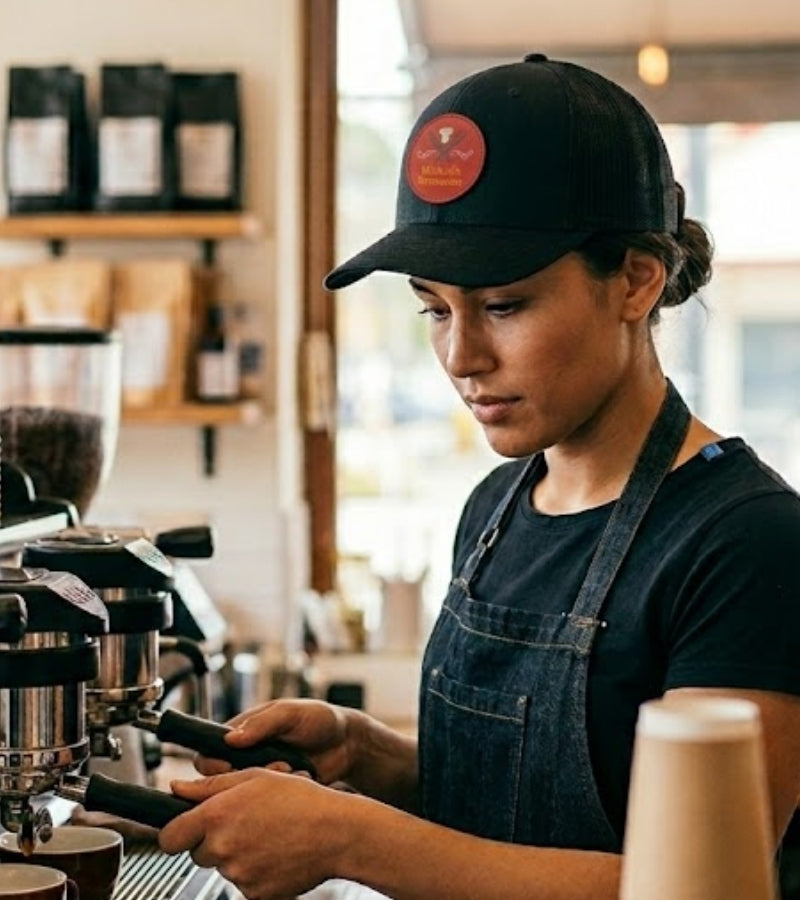 Barista Frau mit schwarzer Cap und Patch mit Klett an Kaffeemaschine